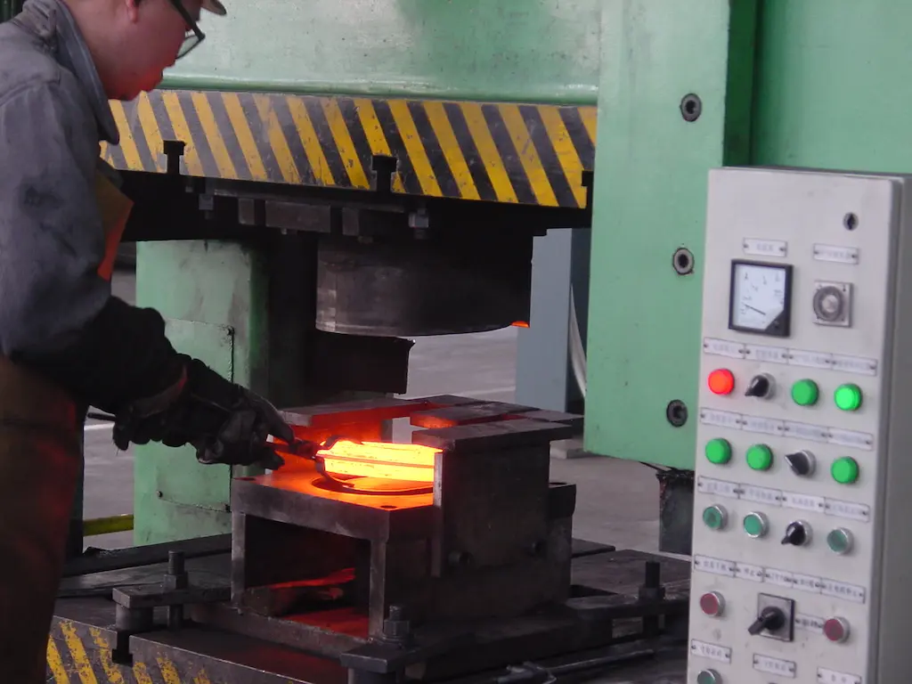 Operator voert warm smeden uit op hydraulische pers bij TOS